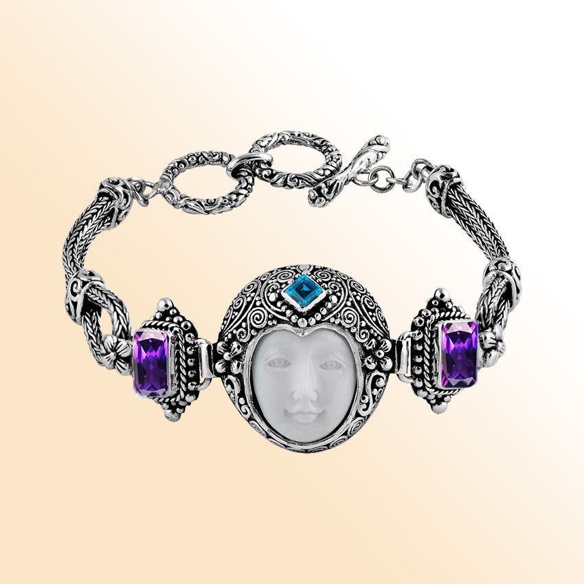 Sterling Silver bracelet featuring an artistic carved bone face centerpiece with Garnet Quartz and Blue Topaz Quartz accents and ornate Balinese scroll detailing.