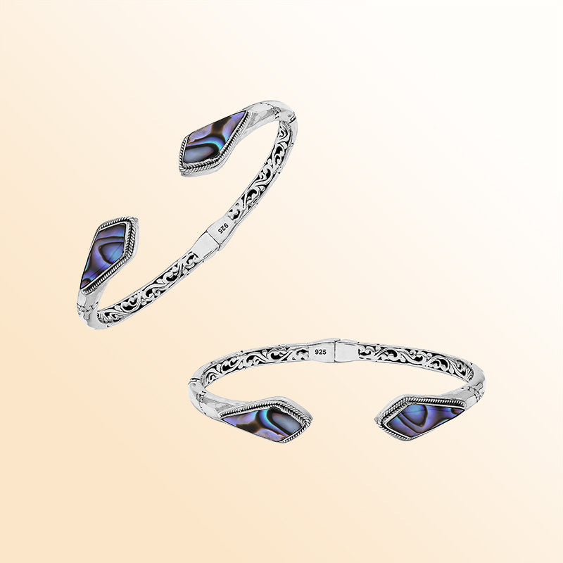 Handcrafted sterling silver bangle featuring Abalone Shell geometric end inlays, ornate Balinese scroll engravings, and a secure hinge lock for elegant, expressive artisan wear.
