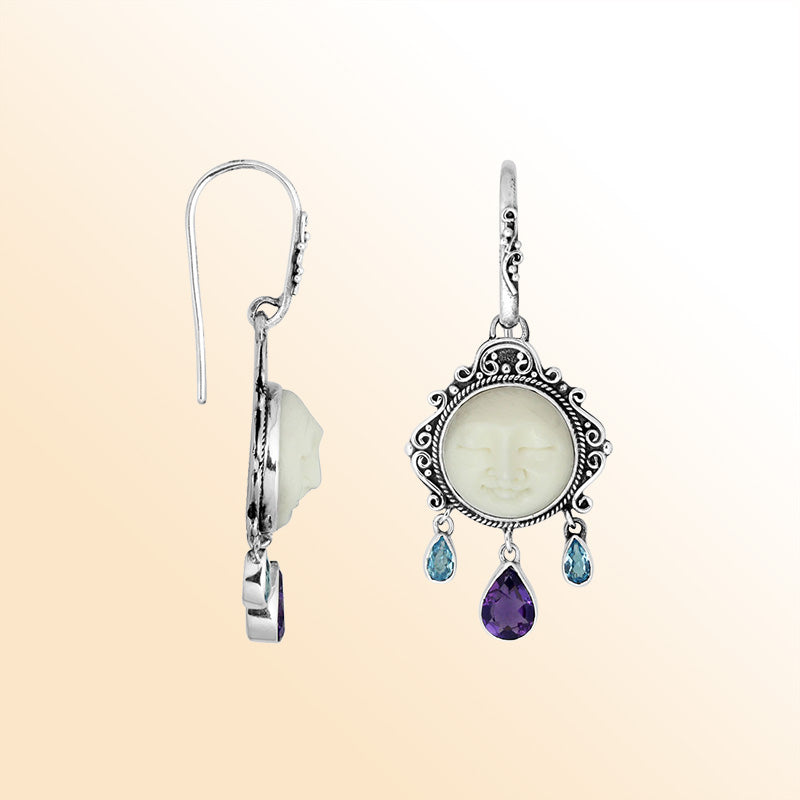 Sterling silver artisan earrings featuring a carved bone face framed with ornate Balinese detailing and accented by blue topaz quartz and amethyst quartz drops for expressive artistic styling.