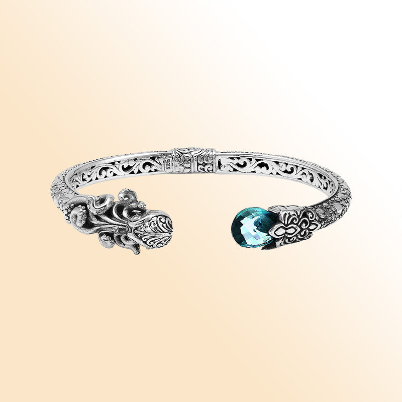A handcrafted sterling silver octopus bangle featuring blue topaz quartz, ornate Balinese carvings, oxidized textures, and a secure hinge lock for elegant statement wear.