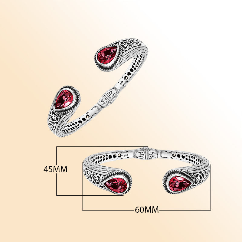 Handcrafted sterling silver bangle with red garnet quartz teardrop stones, ornate Bali engravings, polished shine, and secure hinge lock for elegant daily wear.