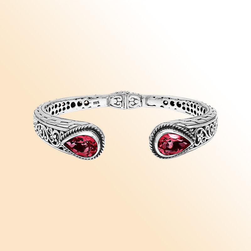 Handcrafted sterling silver bangle with red garnet quartz teardrop stones, ornate Bali engravings, polished shine, and secure hinge lock for elegant daily wear.