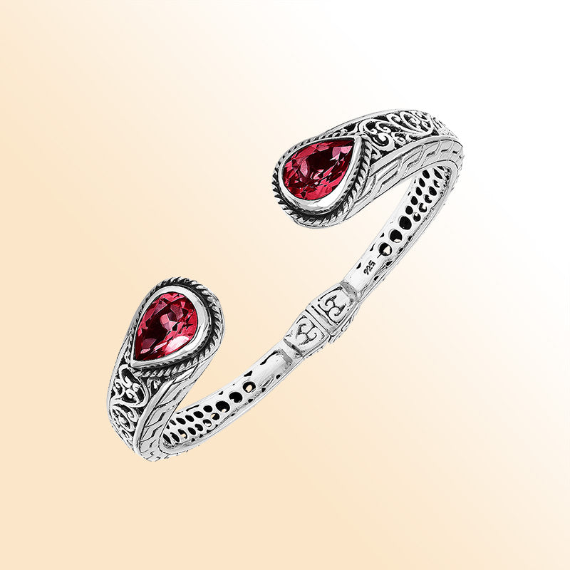 Handcrafted sterling silver bangle with red garnet quartz teardrop stones, ornate Bali engravings, polished shine, and secure hinge lock for elegant daily wear.