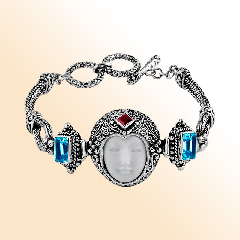 Sterling Silver bracelet showcasing an artistic carved bone face centerpiece with Red Garnet Quartz and Blue Topaz Quartz accents framed by intricate Balinese scrollwork.