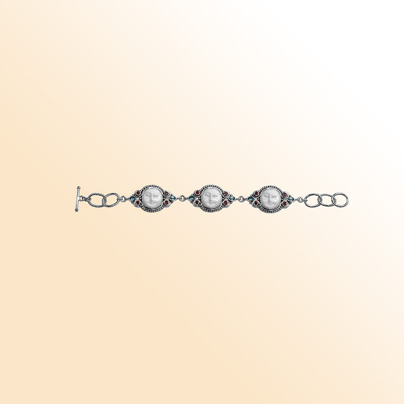Artistic sterling silver bracelet with carved bone faces, Garnet Quartz accents, Blue Topaz Quartz details, and a decorative toggle lock.