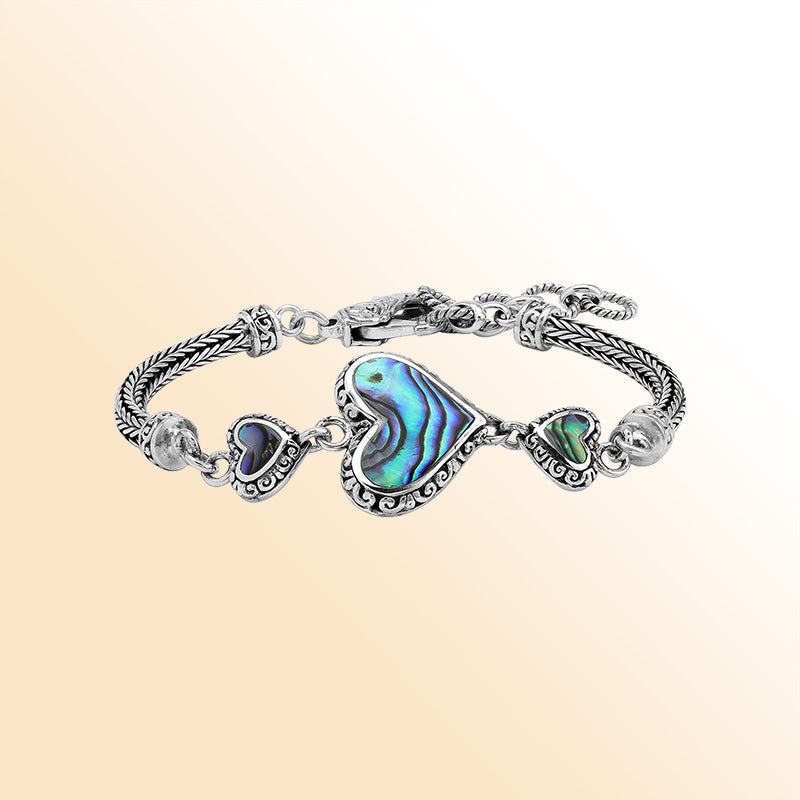 Handcrafted sterling silver bracelet featuring Abalone Shell heart motifs, ornate Balinese scrollwork, and a secure lobster lock for colorful, expressive, artisan-inspired everyday style.