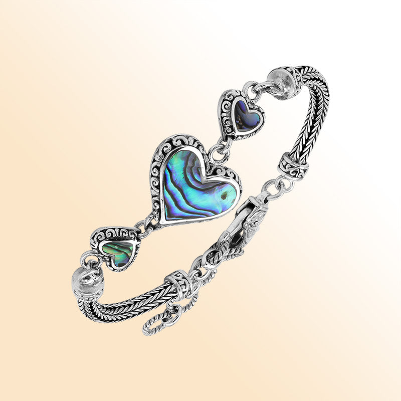 Handcrafted sterling silver bracelet featuring Abalone Shell heart motifs, ornate Balinese scrollwork, and a secure lobster lock for colorful, expressive, artisan-inspired everyday style.