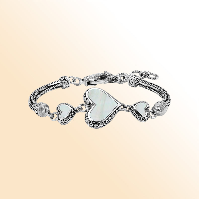 Handcrafted sterling silver bracelet featuring luminous Mother Of Pearl heart motifs, ornate Balinese scroll engravings, and a secure lobster lock for elegant, expressive, artisan-inspired everyday wear.