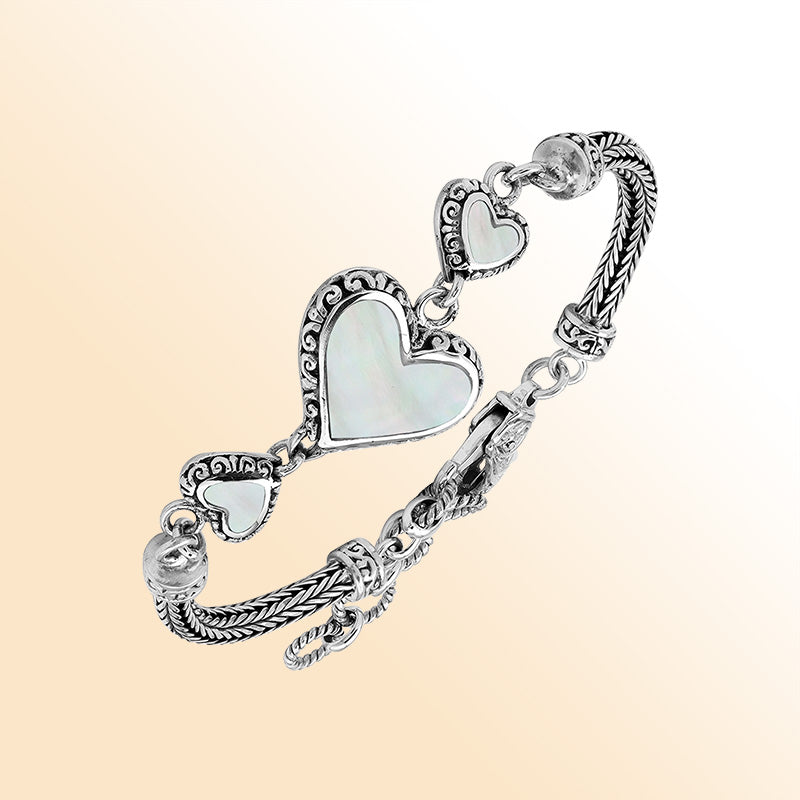 Handcrafted sterling silver bracelet featuring luminous Mother Of Pearl heart motifs, ornate Balinese scroll engravings, and a secure lobster lock for elegant, expressive, artisan-inspired everyday wear.