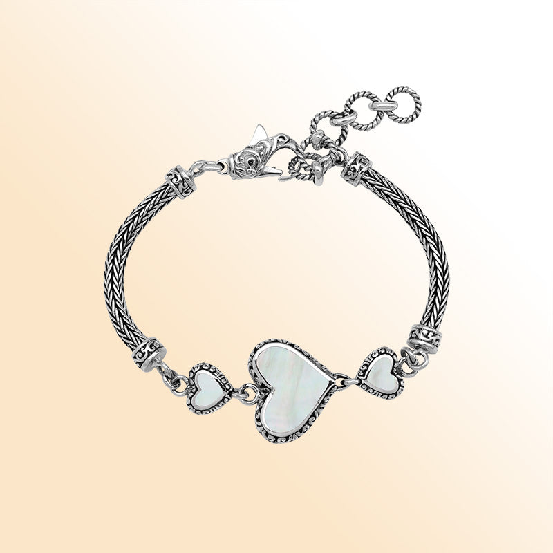 Handcrafted sterling silver bracelet featuring luminous Mother Of Pearl heart motifs, ornate Balinese scroll engravings, and a secure lobster lock for elegant, expressive, artisan-inspired everyday wear.