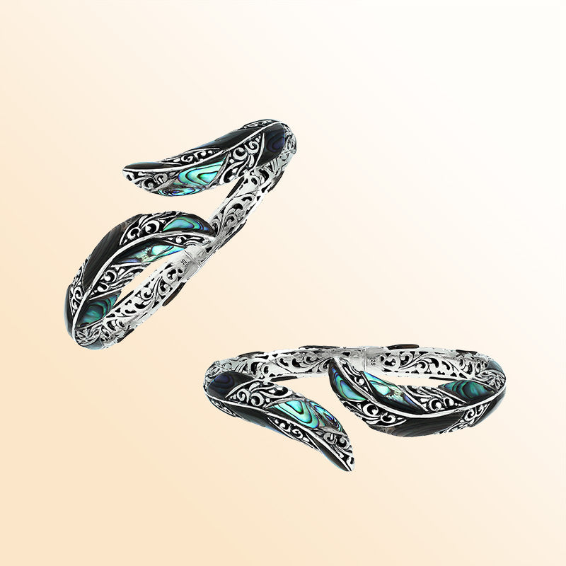 Handcrafted sterling silver feather-inspired bangle featuring luminous Abalone Shell inlays, ornate Balinese scroll engravings, and a secure hinge lock for expressive, artistic everyday wear.