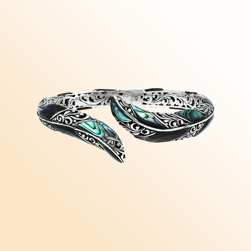 Handcrafted sterling silver feather-inspired bangle featuring luminous Abalone Shell inlays, ornate Balinese scroll engravings, and a secure hinge lock for expressive, artistic everyday wear.
