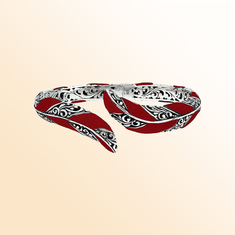 Handcrafted sterling silver feather-inspired bangle featuring vivid Red Coral inlays, ornate Balinese scroll engravings, and a secure hinge lock for expressive, artistic everyday elegance.