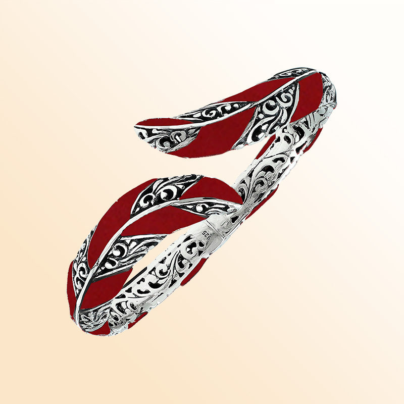Handcrafted sterling silver feather-inspired bangle featuring vivid Red Coral inlays, ornate Balinese scroll engravings, and a secure hinge lock for expressive, artistic everyday elegance.