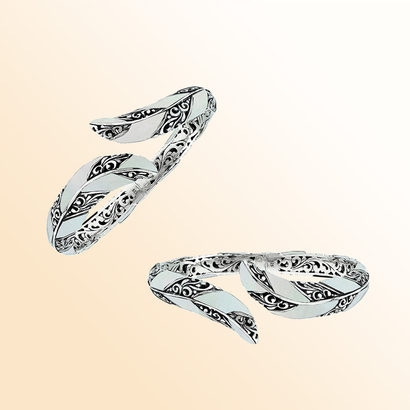 Handcrafted sterling silver feather-inspired bangle featuring luminous Mother Of Pearl inlays, detailed Balinese scroll engravings, and a secure hinge lock for elegant, expressive artisan wear.