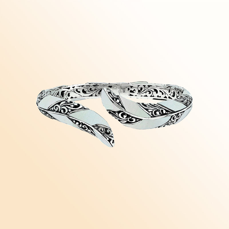 Handcrafted sterling silver feather-inspired bangle featuring luminous Mother Of Pearl inlays, detailed Balinese scroll engravings, and a secure hinge lock for elegant, expressive artisan wear.
