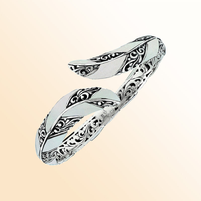 Handcrafted sterling silver feather-inspired bangle featuring luminous Mother Of Pearl inlays, detailed Balinese scroll engravings, and a secure hinge lock for elegant, expressive artisan wear.