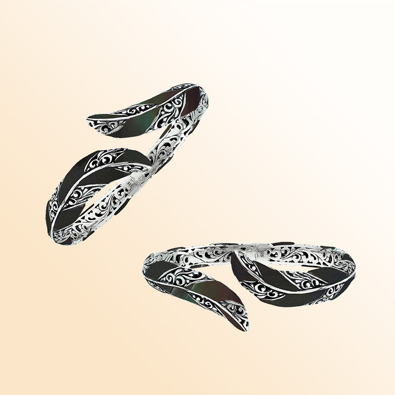 Handcrafted sterling silver feather-inspired bangle featuring bold Black Shell inlays, detailed Balinese scroll engravings, and a secure hinge lock for elegant, expressive artisan-style wear.