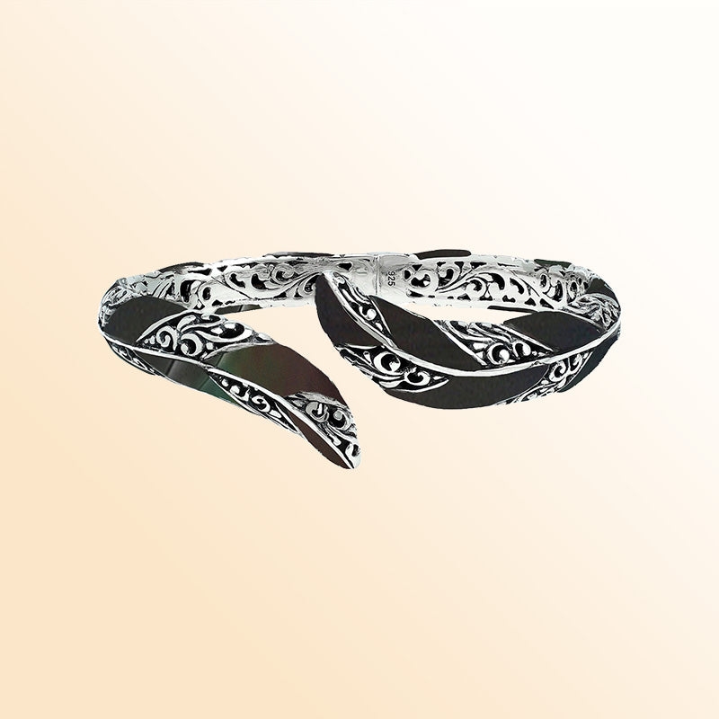 Handcrafted sterling silver feather-inspired bangle featuring bold Black Shell inlays, detailed Balinese scroll engravings, and a secure hinge lock for elegant, expressive artisan-style wear.