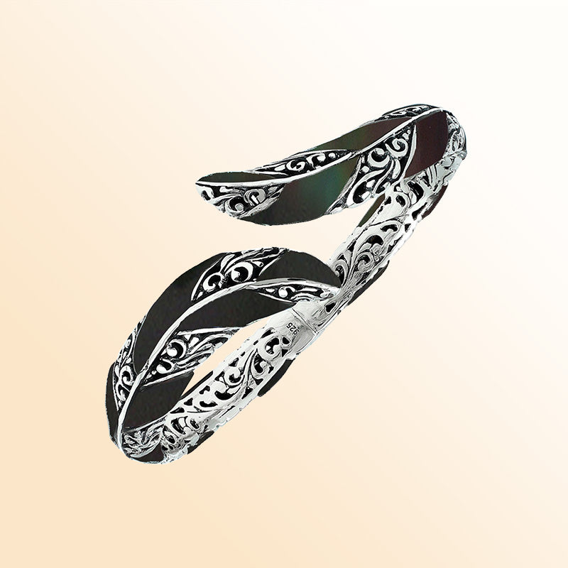 Handcrafted sterling silver feather-inspired bangle featuring bold Black Shell inlays, detailed Balinese scroll engravings, and a secure hinge lock for elegant, expressive artisan-style wear.