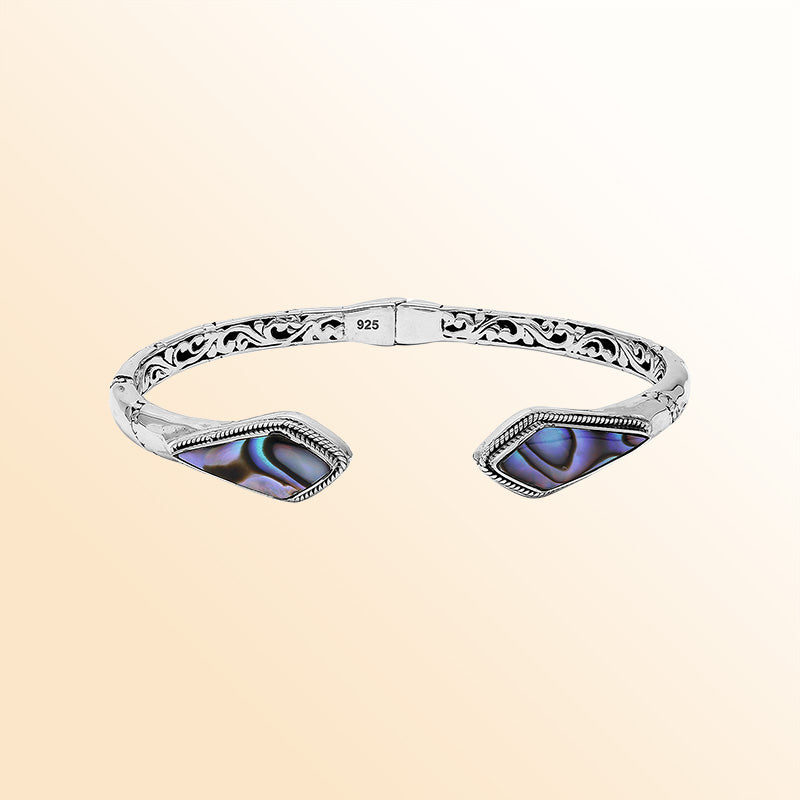 Handcrafted sterling silver bangle featuring Abalone Shell geometric end inlays, ornate Balinese scroll engravings, and a secure hinge lock for elegant, expressive artisan wear.