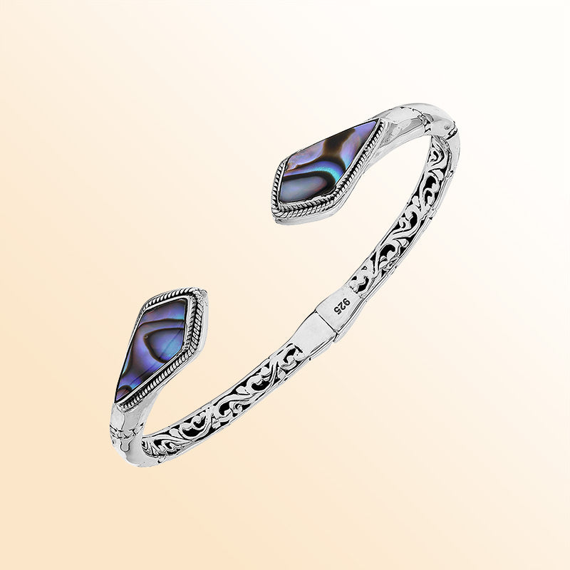 Handcrafted sterling silver bangle featuring Abalone Shell geometric end inlays, ornate Balinese scroll engravings, and a secure hinge lock for elegant, expressive artisan wear.