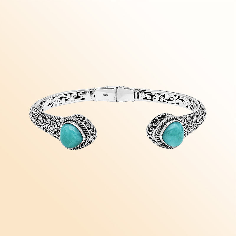 Handcrafted sterling silver bangle featuring two Larimar end stones, ornate Balinese scroll engravings, and a secure hinge lock for elegant, artisan-inspired everyday wear.