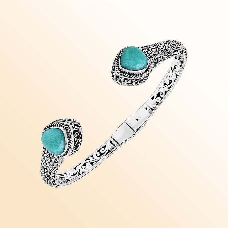 Handcrafted sterling silver bangle featuring two Larimar end stones, ornate Balinese scroll engravings, and a secure hinge lock for elegant, artisan-inspired everyday wear.