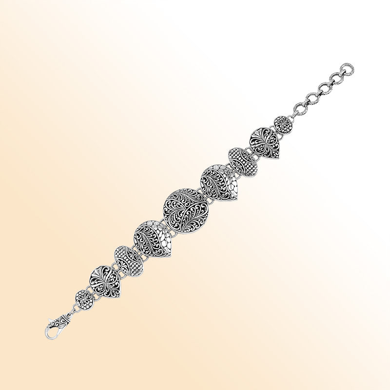Handcrafted sterling silver link bracelet featuring carved Balinese scrollwork motifs across multiple shapes with oxidized details and a secure lobster lock closure.