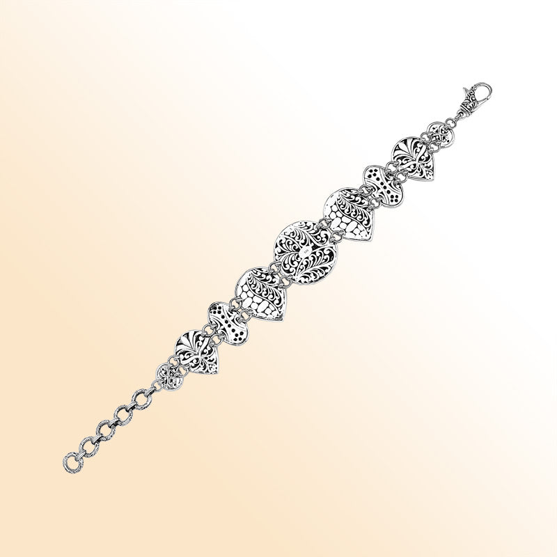 Handcrafted sterling silver link bracelet featuring carved Balinese scrollwork motifs across multiple shapes with oxidized details and a secure lobster lock closure.