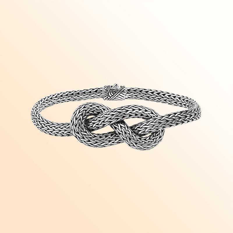 Handcrafted sterling silver bracelet featuring an elegant woven knot centerpiece, detailed chain texture, and a secure push clasp for stylish everyday or special-occasion wear.