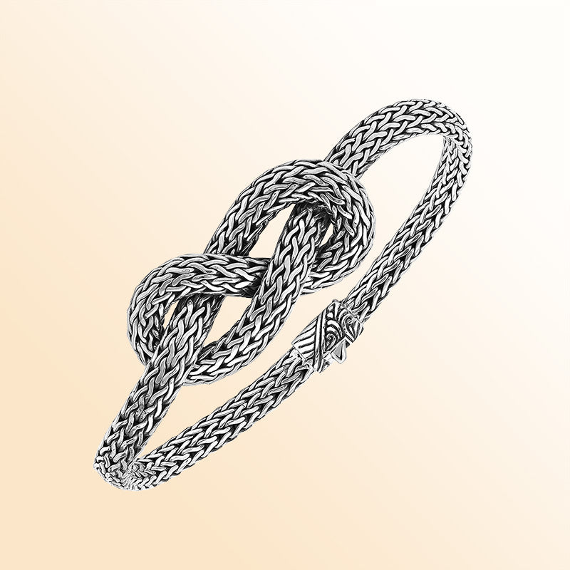 Handcrafted sterling silver bracelet featuring an elegant woven knot centerpiece, detailed chain texture, and a secure push clasp for stylish everyday or special-occasion wear.