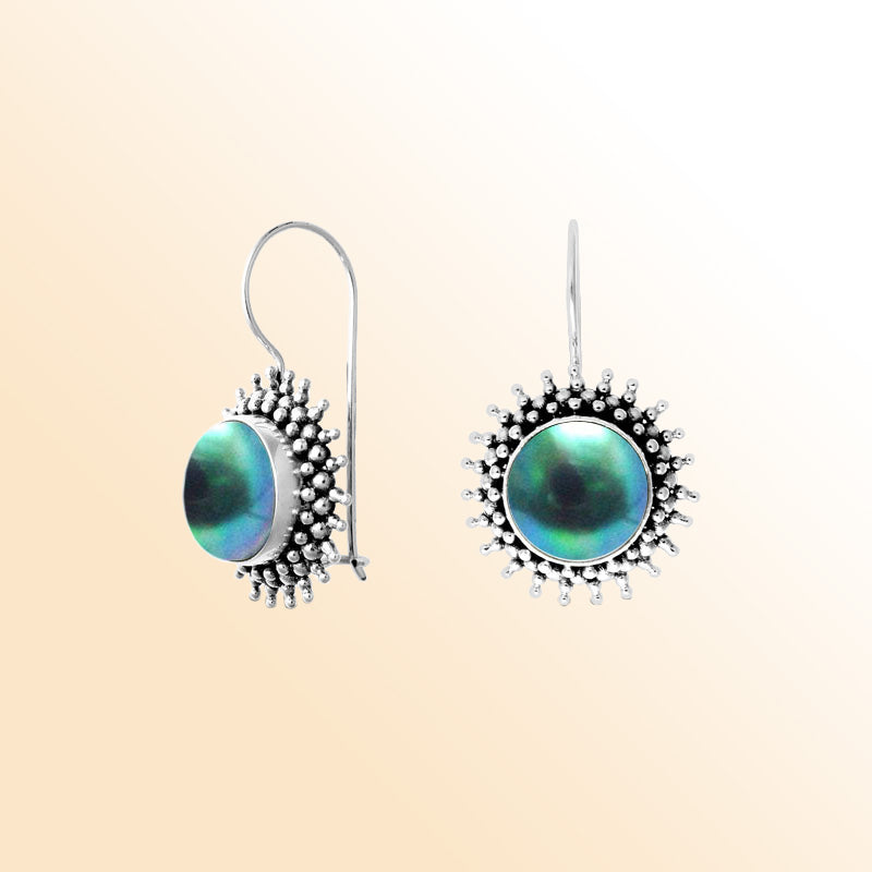 Hand-polished sterling silver earrings featuring luminous green Mabe Pearls set within a detailed sunburst design, completed with artisan-crafted earwire hooks.