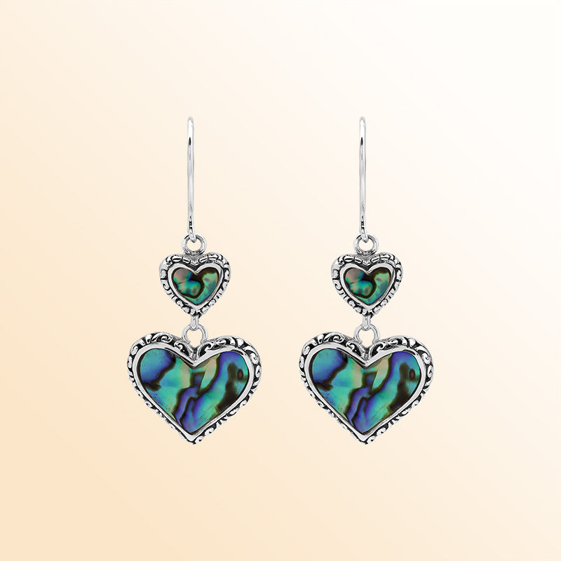 Sterling silver artisan earrings featuring shimmering double abalone shell hearts with ornate decorative borders, crafted to evoke a romantic ocean-inspired look for expressive and elegant everyday wear.