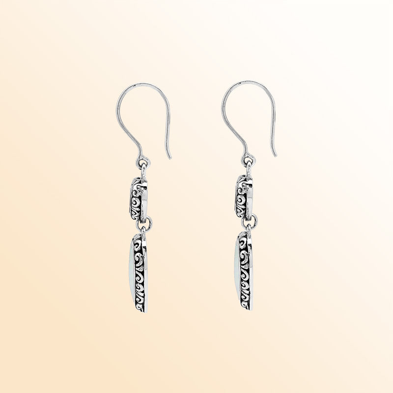 Sterling silver artisan earrings featuring luminous double mother of pearl hearts with ornate borders, designed to create a romantic and expressive look for elegant everyday wear.