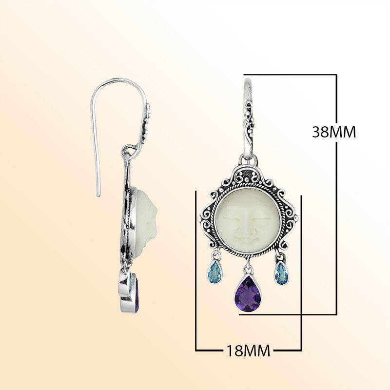 Sterling silver artisan earrings featuring a carved bone face framed with ornate Balinese detailing and accented by blue topaz quartz and amethyst quartz drops for expressive artistic styling.