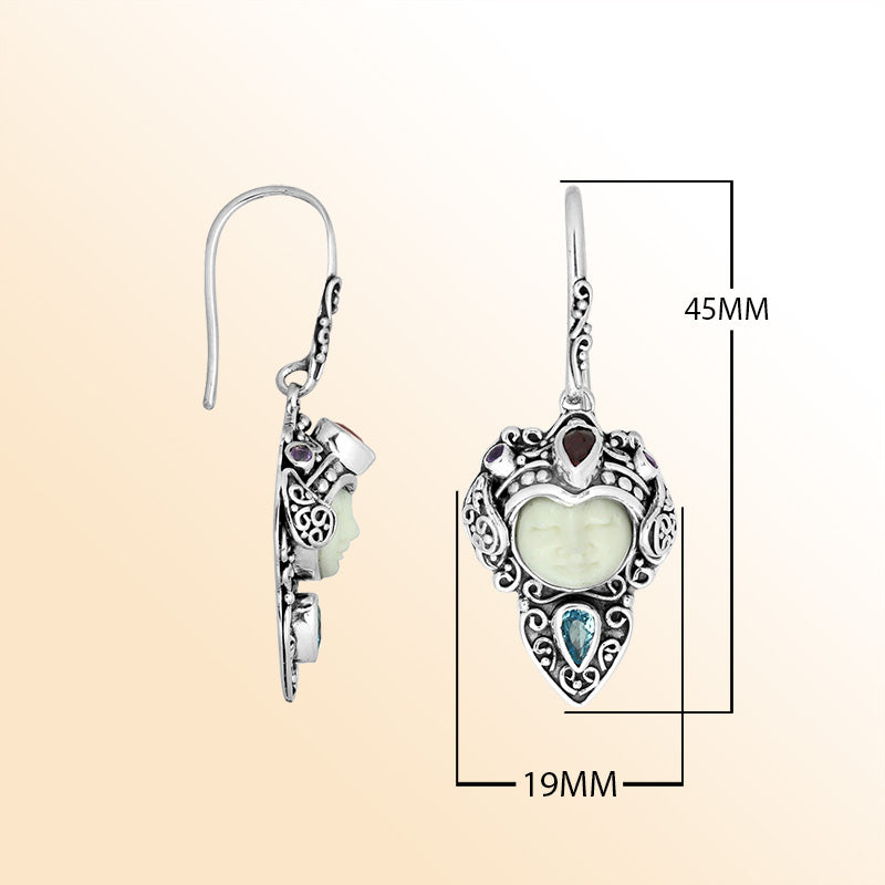 Sterling silver artisan earrings featuring a serene Bone Face carving paired with Blue Topaz Quartz and Garnet Quartz stones, surrounded by ornate Balinese scrollwork for expressive personal styling.
