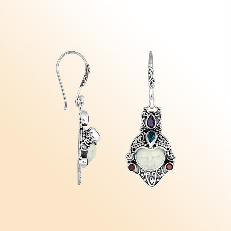 A stunning pair of 925 sterling silver earrings featuring carved bone faces with detailed Balinese filigree and Amethyst Quartz, Blue Topaz Quartz, and Garnet Quartz stones.