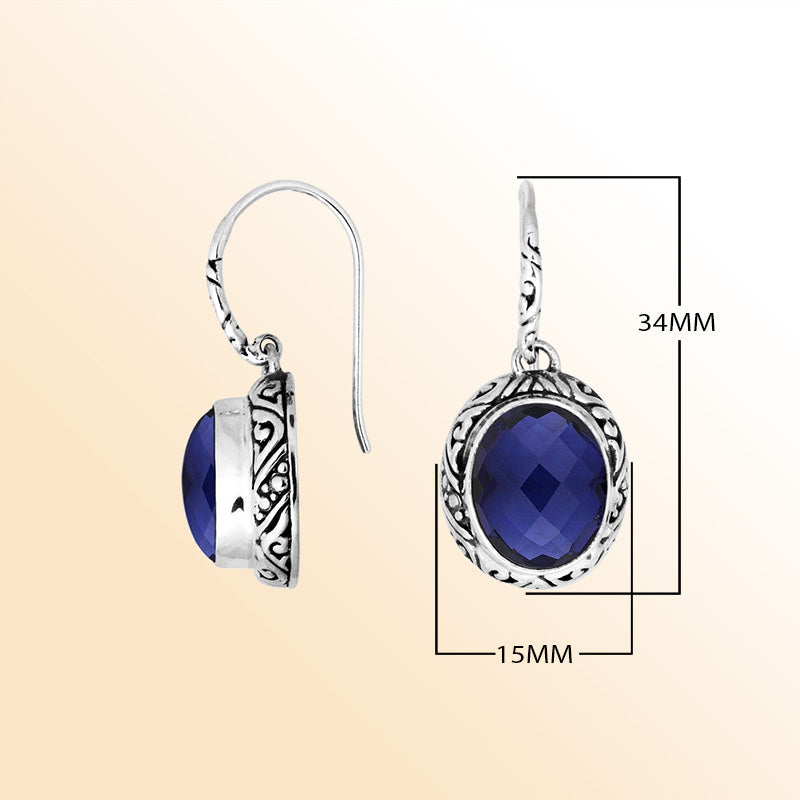 Sterling silver earrings featuring a deep-blue faceted oval Sapphire stone framed with ornate carved detailing and earwire lock, offering expressive color and handcrafted elegance for elevated everyday wear.