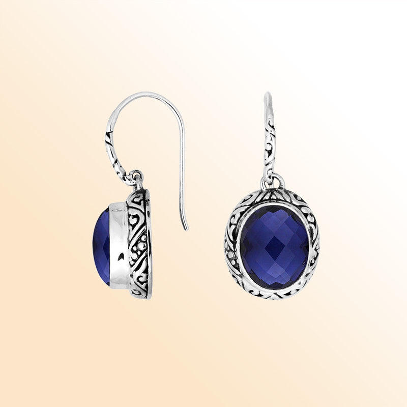 Sterling silver earrings featuring a deep-blue faceted oval Sapphire stone framed with ornate carved detailing and earwire lock, offering expressive color and handcrafted elegance for elevated everyday wear.