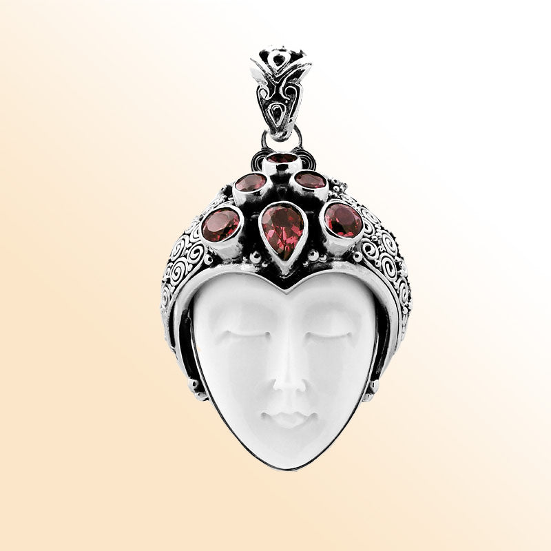 Handcrafted sterling silver pendant featuring a serene goddess face carved from bone with sparkling garnet gemstones, unique Balinese artisan jewelry for women.