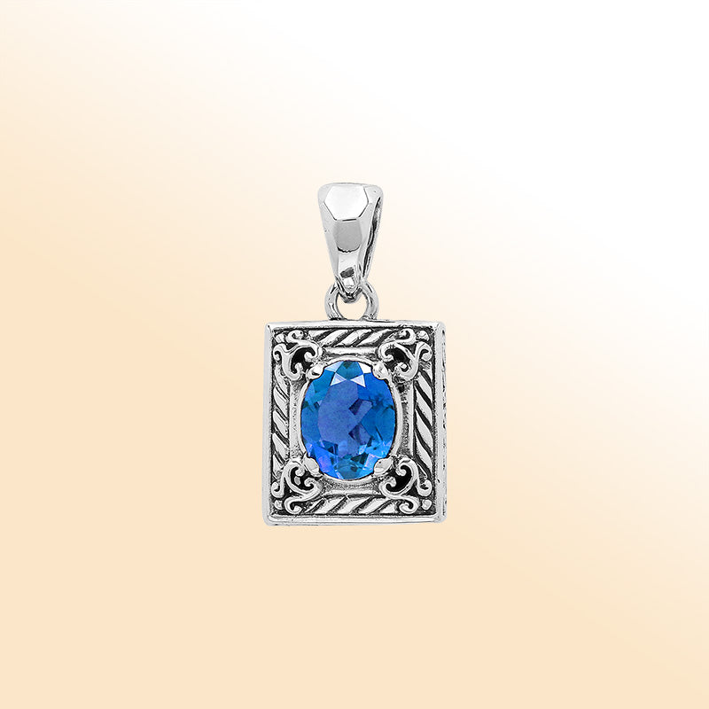 Handcrafted sterling silver pendant with oval blue topaz quartz, ornate swirl engraving, and polished finish showcasing fine Balinese artistry.
