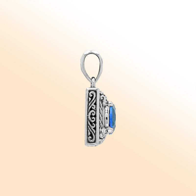 Handcrafted sterling silver pendant with oval blue topaz quartz, ornate swirl engraving, and polished finish showcasing fine Balinese artistry.