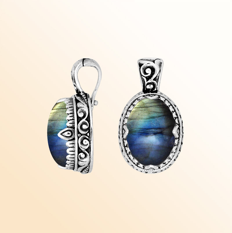 A handcrafted sterling silver pendant showcasing an iridescent Labradorite centerpiece accented with artistic Balinese scroll carvings and a smooth decorative frame for expressive personal styling.