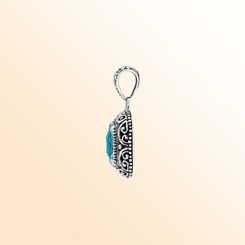 Handcrafted sterling silver cushion pendant featuring a faceted Blue Topaz Quartz centerpiece highlighted by artistic Balinese scroll carvings and a smooth decorative frame.